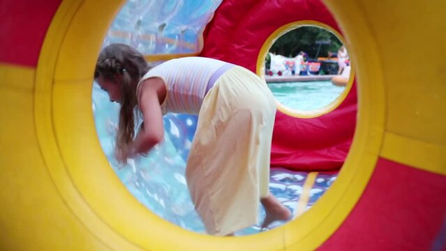 Happy girl in dress runs in big inflatable cylinder on water