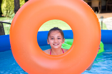 Fototapeta na wymiar Portrait of cute little girl in swimming pool with orange inflatable ring