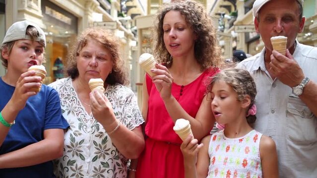 Happy family of five stand in mall ant eat sweet ice cream