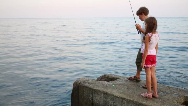 Boy teen and girl in shorts with fishing rod fishing in blue sea