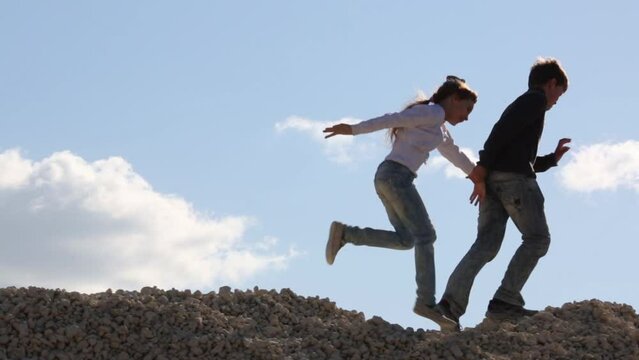 Girl and boy in jeans go on stone pile. Boy drags girl