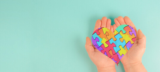 ASD autism spectrum disorder, deficits in social communication and interaction, hands holding heart with colorful jigsaw or puzzle pieces - obrazy, fototapety, plakaty