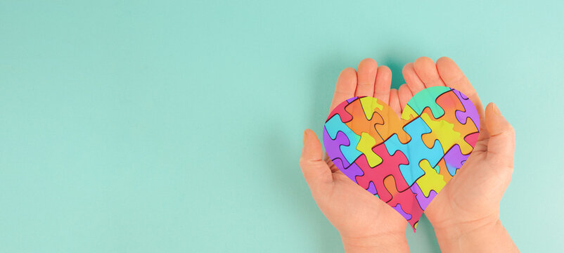 ASD autism spectrum disorder, deficits in social communication and interaction, hands holding heart with colorful jigsaw or puzzle pieces