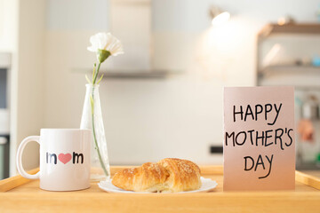 Mother's day still life with mom cup, a sweet pastry and a greeting card on a tray, in airy indoor background.