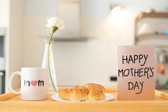 Mother's day still life with mom cup, a sweet pastry and a greeting card on a tray, in airy indoor background.