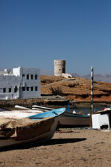 Fototapeta na wymiar Small fishing boats on the shore of the Sur lagoon with ths Al Ayjah watchtower in the background.