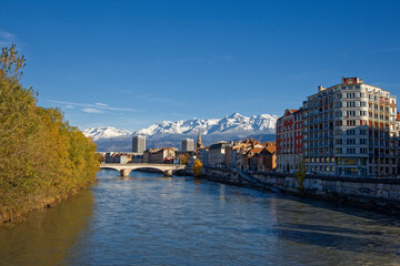 Fototapeta na wymiar GRENOBLE, FRANCE, November 29, 2023 : Isere river and Grenoble city center with snowy mountains landscape in the background