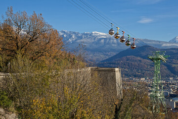 Obraz premium GRENOBLE, FRANCE, November 29, 2023 : The Bubbles cable-car climbs the hill of La Bastille with snowy mountains landscape in the background