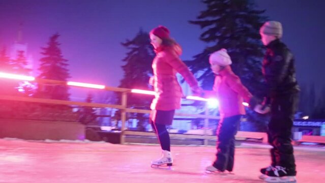 Mother and two children skates at rink holding hands