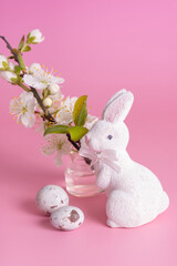 White rabbit, blossom twig and Easter eggs on a pink background. Easter hunt minimalistic composition