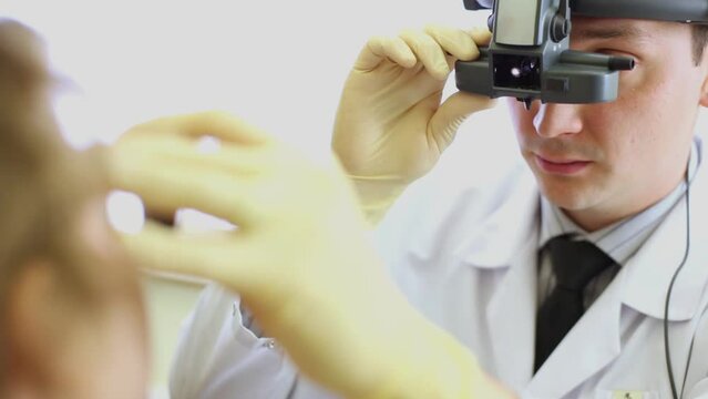 Ophthalmologist with indirect ophthalmoscope inspects girl eye.