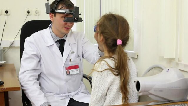 Ophthalmologist examines girl eye through ophthalmoscope.