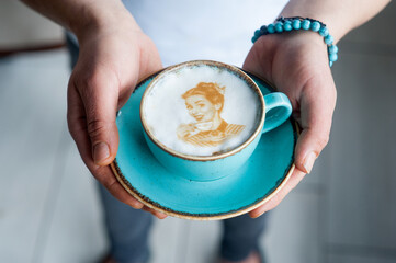 Male hands holding a blue cup of coffee decorated with latte art created with a printer