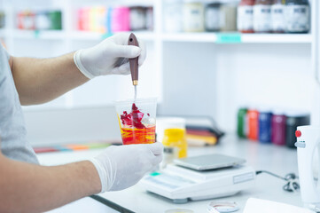 Male hands with a spatula and protective gloves mixing dyes in a plastic container research and...