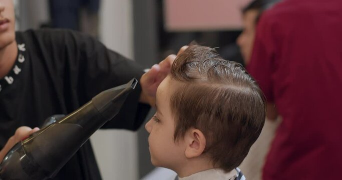 Soft focus Hairdresser cuts hair, combs and blow-dries it. Stylish boy sitting in hairdresser. Barber man cuts hair of cute little boy child. Attractive man getting his hair cut in modern barbershop.