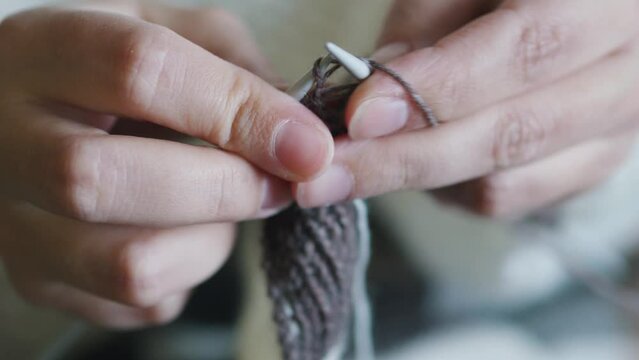 Female caucasian hands knitting brown wool scarf with knitting needles.