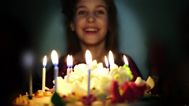 Smiling little girl blows out candles on birthday cake.