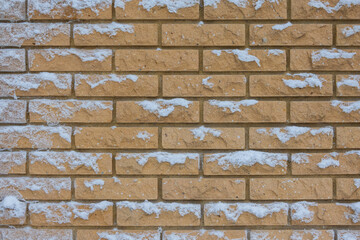 Fragment of a wall made of yellow decorative brick. Flakes of fresh snow stuck to the vertical surface. Background. Texture. Form.