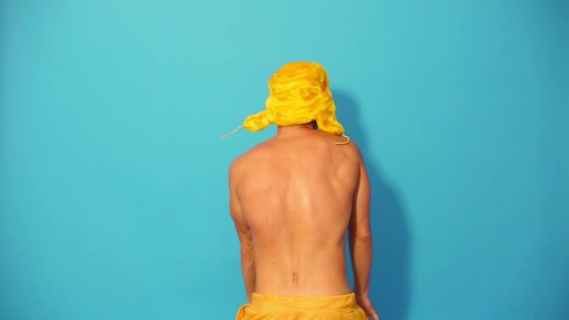 Back of half-naked man in yellow cap dancing in blue studio