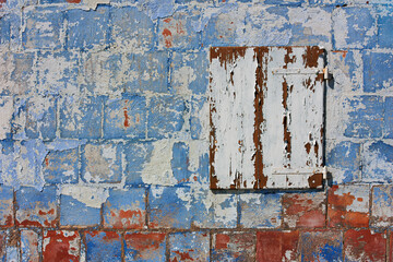 Old wall with peeling paint and closed white window. Colored background of house with scratched blue plaster. - 711831955