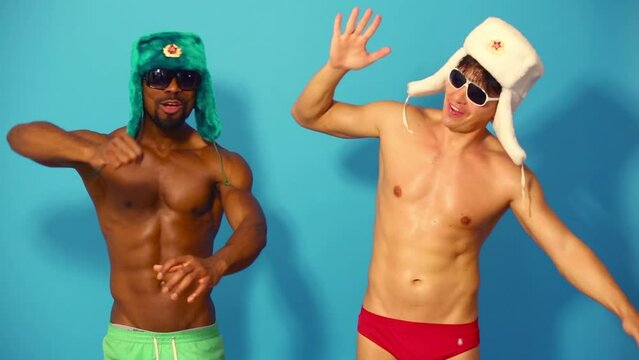 Two white and black half-naked men in caps and sunglasses dance 