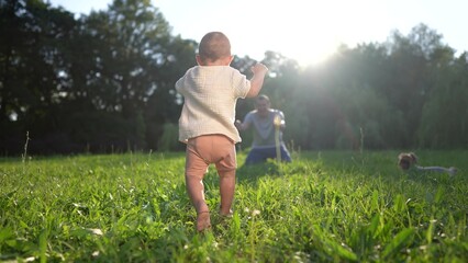 baby takes first steps in the park. happy family kid dream concept. dad teaches his son to walk...