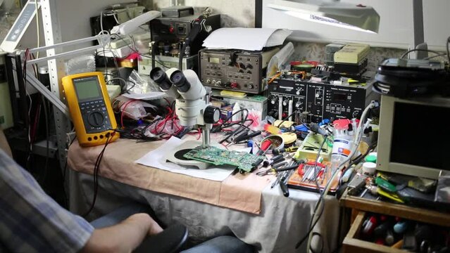 Man looks at motherboard through microscope among tools