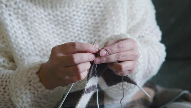Female caucasian hands knitting brown wool scarf with knitting needles.