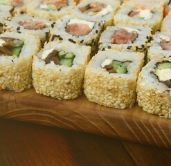 Close-up of a lot of sushi rolls with different fillings lie on a wooden surface. Macro shot of cooked classic Japanese food with a copy space.
