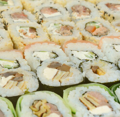 Close-up of a lot of sushi rolls with different fillings lie on a wooden surface. Macro shot of cooked classic Japanese food with a copy space.