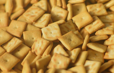 A lot of small cookies are square shaped. A pattern of a yellow salt cracker. Background image with salted pastry
