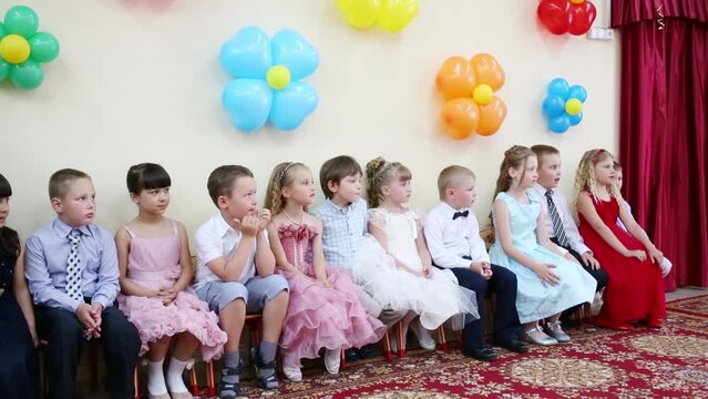 Twelve little boys and girls sit in hall decorated with balloons
