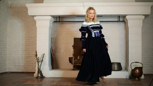 Pretty woman in medieval costume dances near fireplace