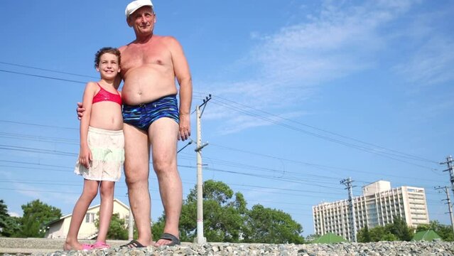 A man and his granddaughter in swimwear stands on the mound