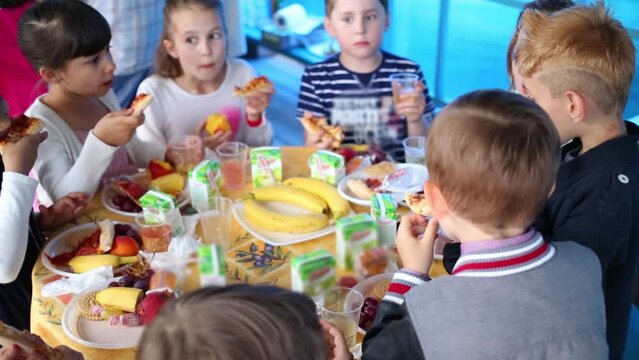 Eight happy children eats sweets at festive table in kindergarten