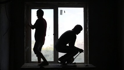 Silhouettes of two workers who dismantle old window frame. - Powered by Adobe
