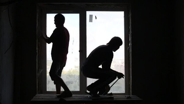 Silhouettes of two workers who dismantle old window frame.