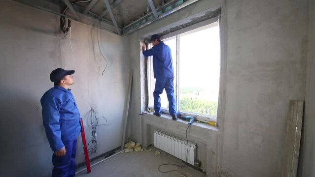 Two workers install window frame and check vertical accuracy