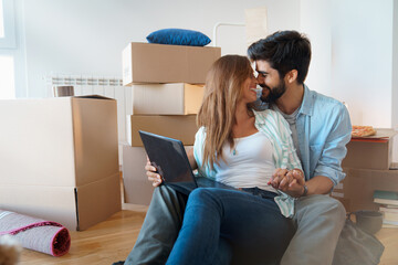 Young contemplative couple sitting on floor and thinking about their future while looking face to face. Happy married couple buy new apartment and plan a family. Couple in new home using laptop.