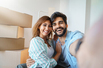 Young man and woman sitting on floor and taking selfie at new home. Splendid young smiling couple...