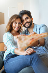 Cheerful couple in love eating pizza on a break from home renovation process. Beautiful young woman...