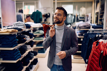 Young smiling man shopping in clothing store. - obrazy, fototapety, plakaty