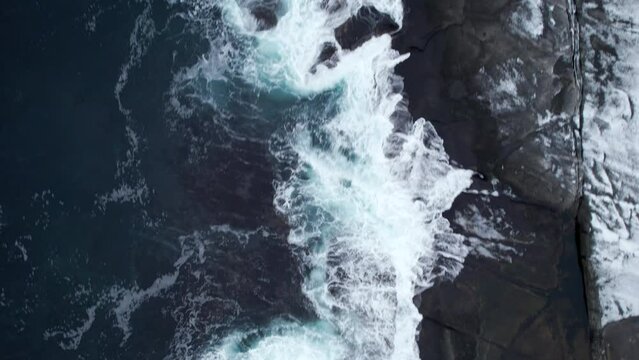 Top-down aerial shot of cold arctic ocean waves hitting rocky shoreline, forward movement