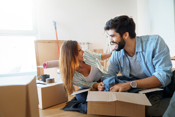 Couple after moving in a new home unboxing their items. Couple sitting together on floor looking at...