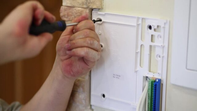 Male hands turn screw to fix back panel of intercom at wall.