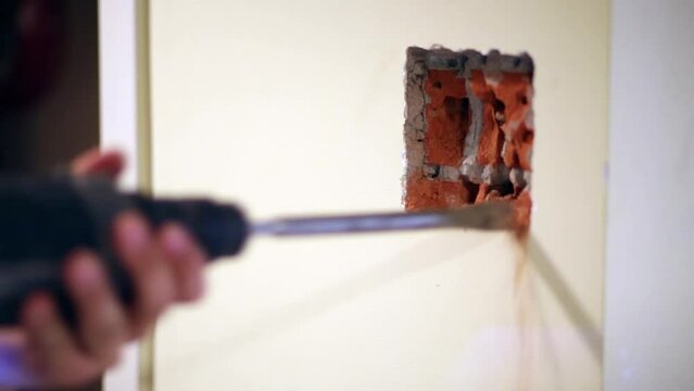 Worker makes hollow in brick under plaster on wall 