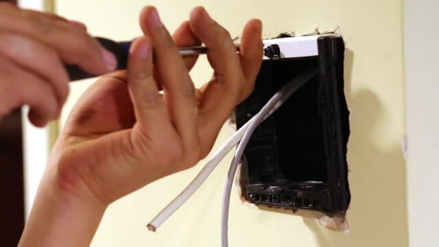 Worker hands twist screw fixing mounting box into hollow in wall.