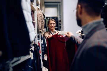Happy woman assisting her boyfriend in choosing clothes while shopping together.
