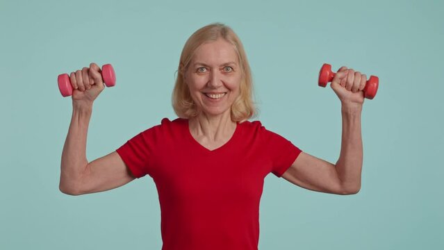 Active senior woman posing with dumbbells in hands and siling . studio shot 
