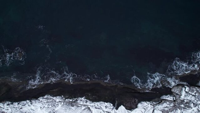Top-down aerial shot of cold arctic ocean waves hitting rocky shoreline, move right